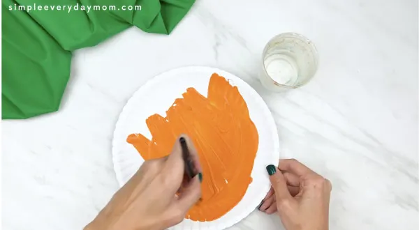 Hands painting paper plate orange