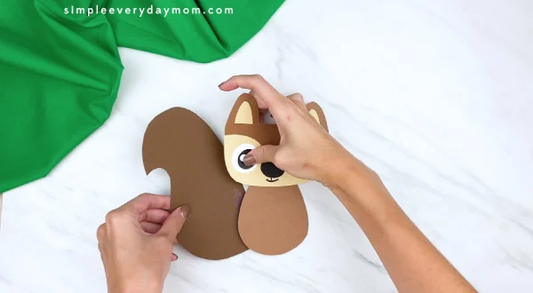 hands gluing paper squirrel tail to back of body