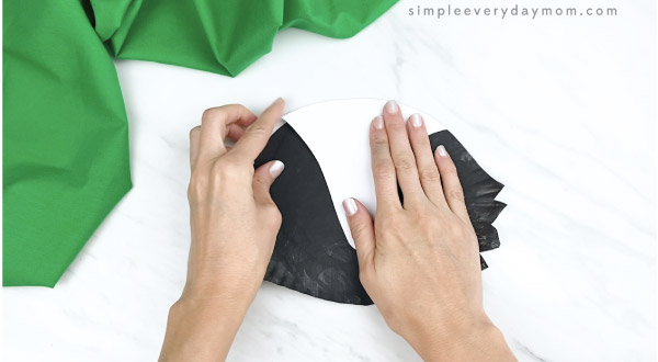 hands gluing stripe onto paper plate skunk