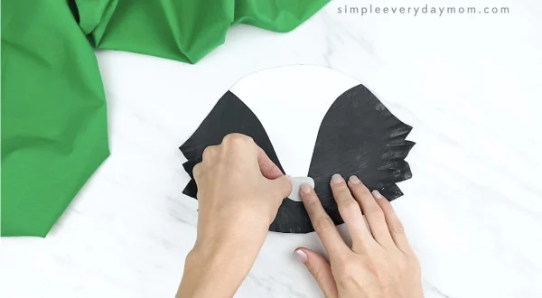 hands gluing nose onto paper plate skunk