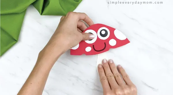 hands gluing stalk to bottom of paper mushroom craft