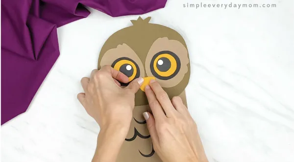 hands gluing beak onto paper bag owl