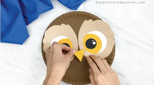 hands gluing beak to paper plate owl craft