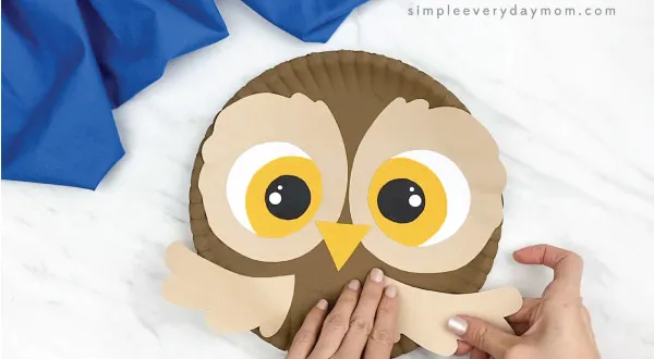 hands gluing wings to paper plate owl craft