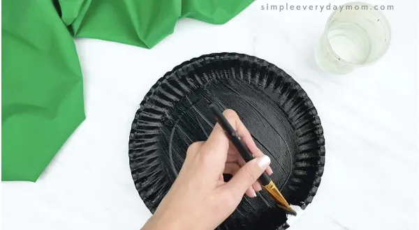 hands painting paper plate black