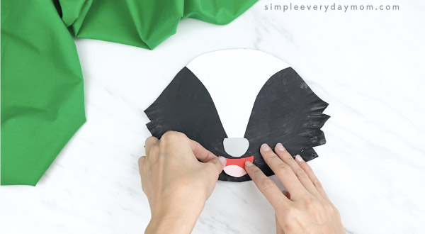 hands gluing nose onto paper plate skunk craft