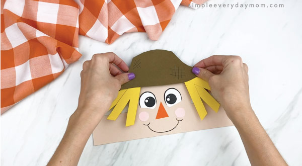hands gluing hat onto scarecrow headband