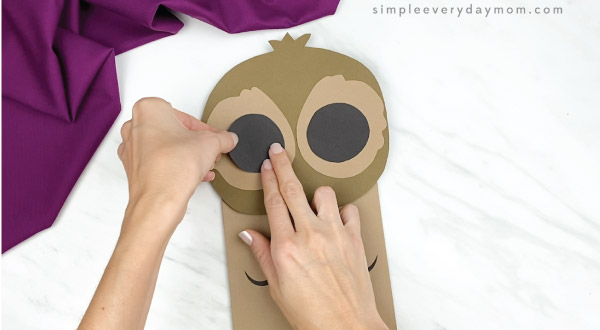 hands gluing black circle onto paper bag owl
