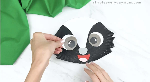 hands gluing eyes onto paper plate skunk craft