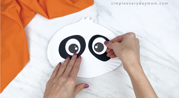 hands gluing eyes to paper plate panda craft