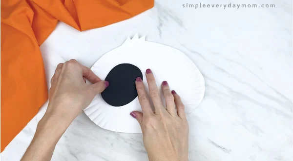 hands gluing black eye area to paper plate panda craft