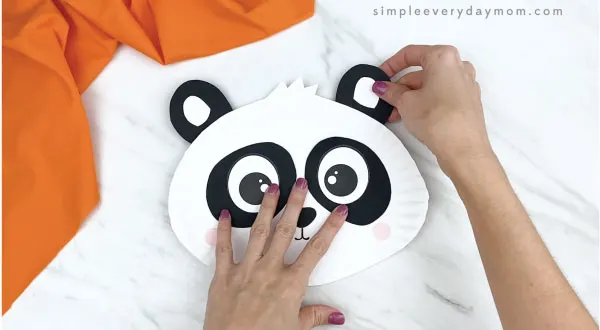 hands gluing ears to paper plate panda craft