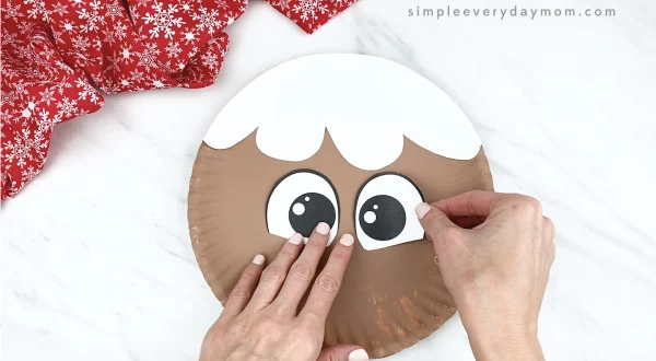 hands gluing bow to eyes paper plate gingerbread craft