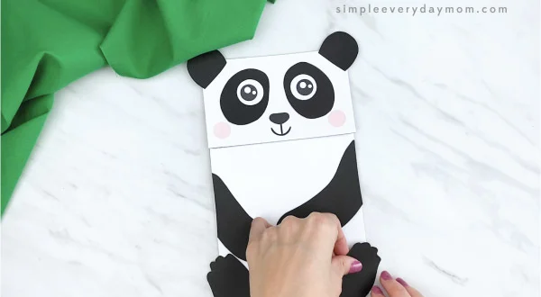 hands gluing feet to paper bag panda craft