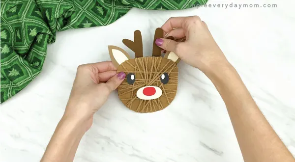 hands gluing antlers to yarn wrapped reindeer craft