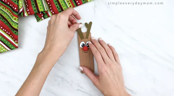 hands gluing antlers on popsicle stick reindeer