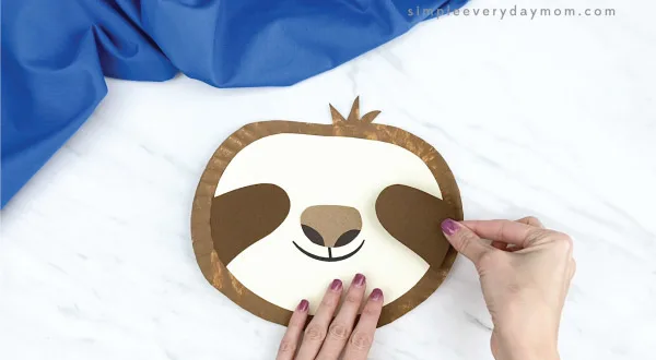 hands gluing eye area to paper plate sloth craft