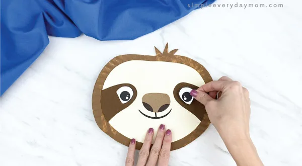 hands gluing eye to paper plate sloth craft