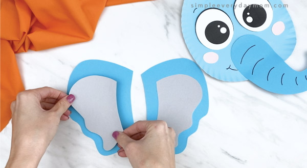 hands gluing inner ear to outer ear of paper plate elephant craft