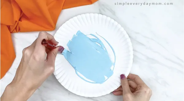 hands painting paper plate light blue