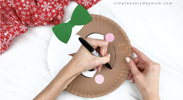 hands drawing smile onto paper plate gingerbread girl craft