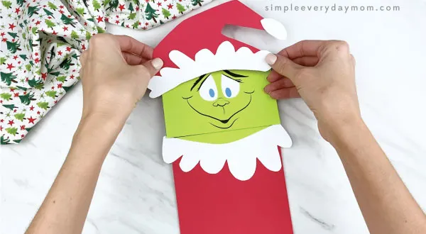 hands gluing Santa hat onto paper bag Grinch