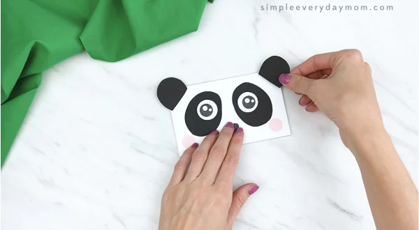 hands gluing ears to paper bag panda craft