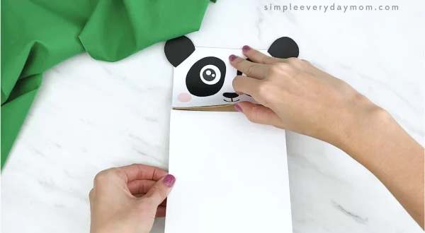 hands gluing white paper to paper bag panda craft