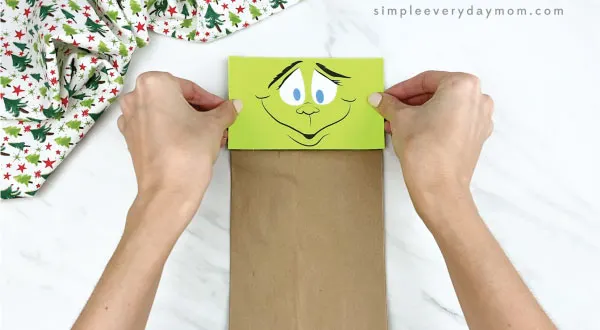 hands gluing face onto paper bag Grinch