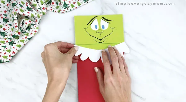 hands gluing Santa suit trim onto paper bag Grinch