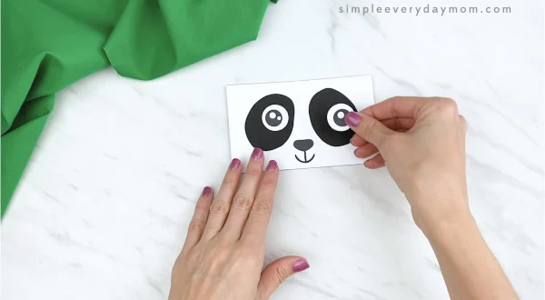 hands gluing eyes to paper bag panda craft