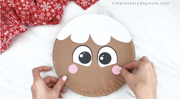 hands gluing cheeks to girl paper plate gingerbread craft