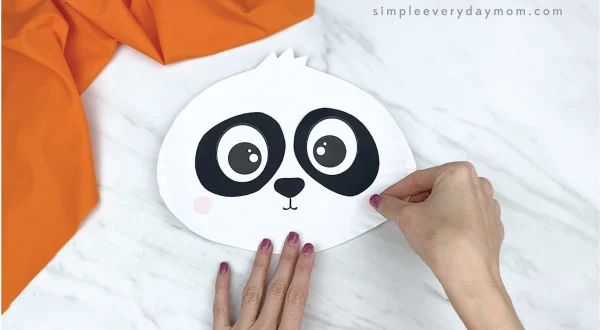 hands gluing cheeks to paper plate panda craft