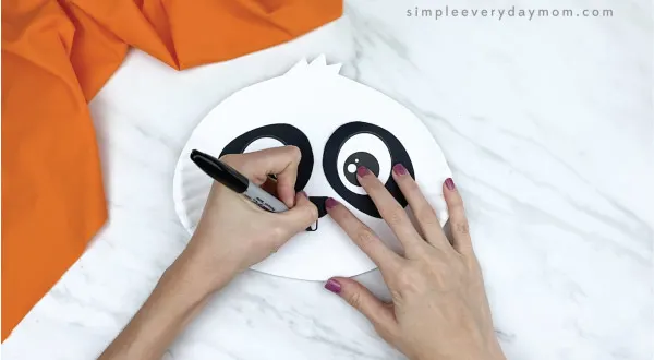 hands drawing mouth onto paper plate panda craft