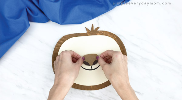 hands gluing nose to paper plate sloth craft