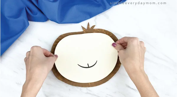 hands gluing face to paper plate sloth craft