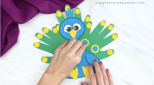 hands adding feather details to handprint peacock craft