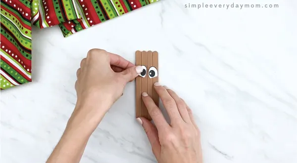 hands gluing eyes on popsicle stick reindeer