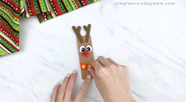 hands gluing yellow pom poms on popsicle stick reindeer