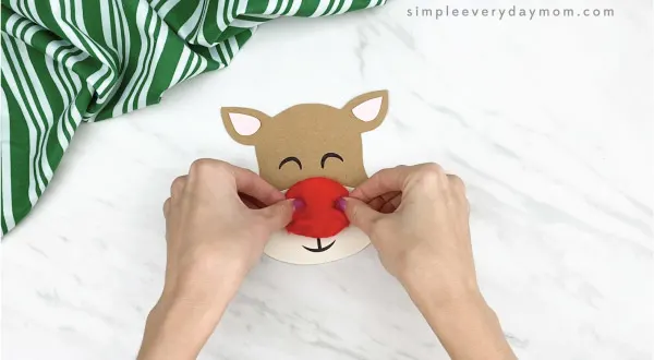 hands gluing pom pom nose to clothespin reindeer craft