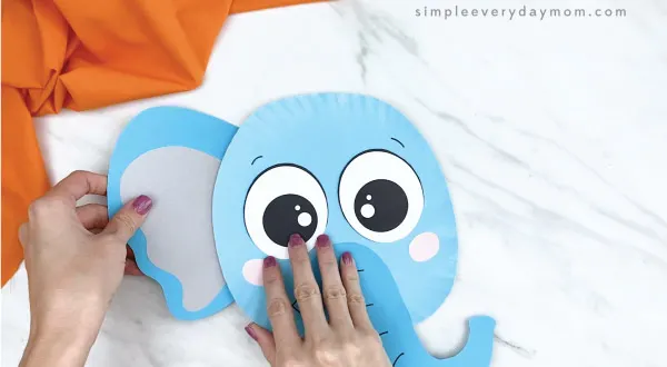 hands gluing ears onto paper plate elephant craft