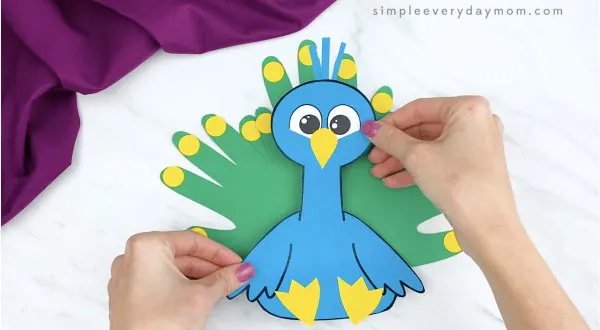 hands gluing body onto handprint peacock craft