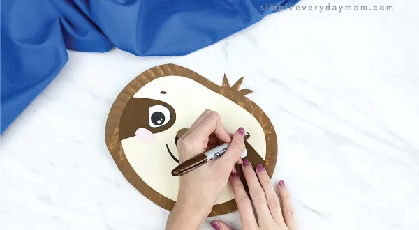 hands drawing eyebrows onto paper plate sloth