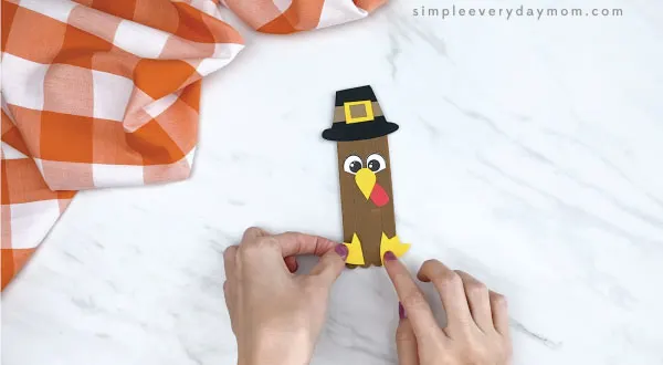 hands gluing feet onto popsicle stick turkey craft