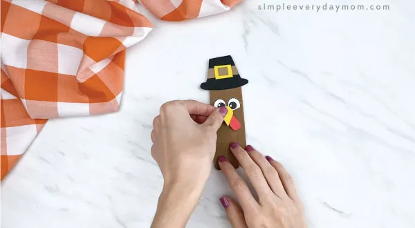 hands gluing beak onto popsicle stick turkey craft
