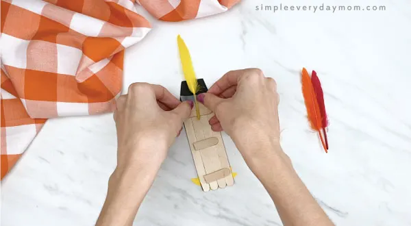 hands gluing feathers onto popsicle stick turkey craft
