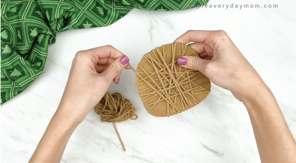 hands wrapping brown yarn around cardboard