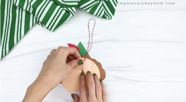 hands taping baker's twine loop to back of elf ornament craft