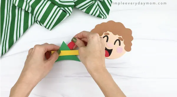 hands gluing feather to paper elf hat