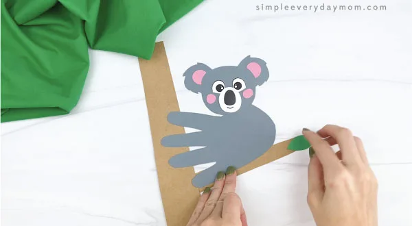 hands gluing leaves to handprint koala craft